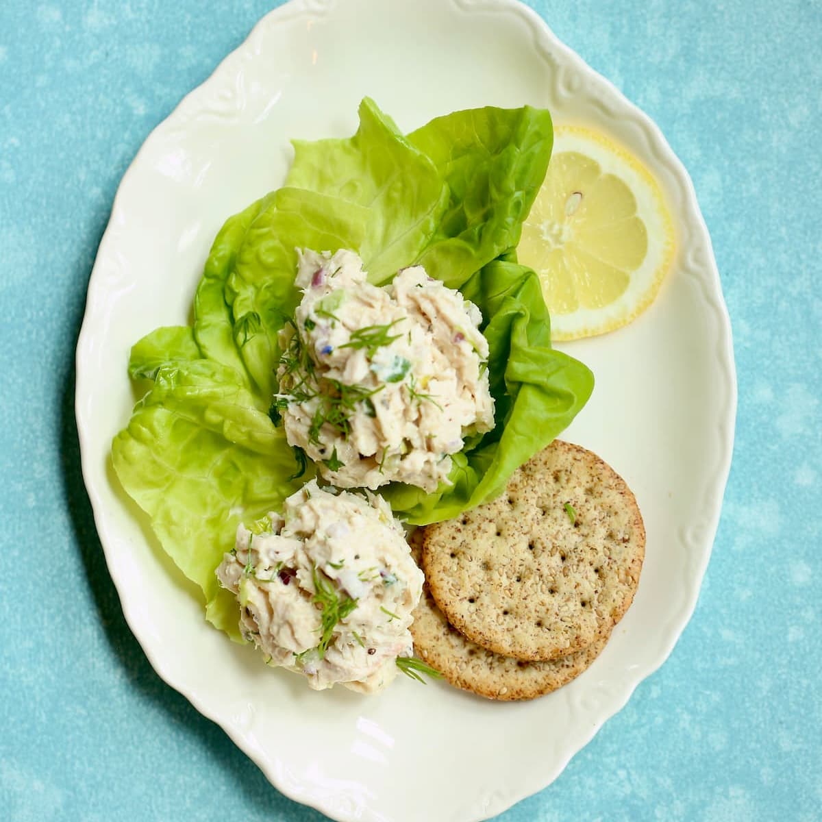 A square image of a white plate with chicken salad in lettuce cups with crackers.