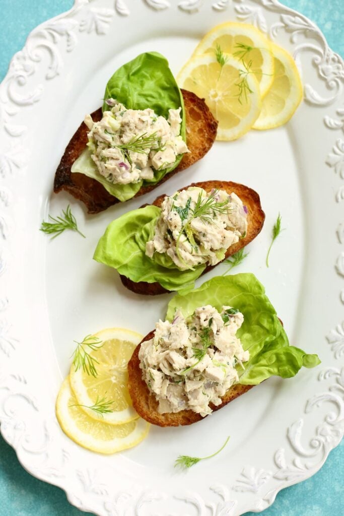 A white platter of three chicken salad sandwiches on toasted bread. 