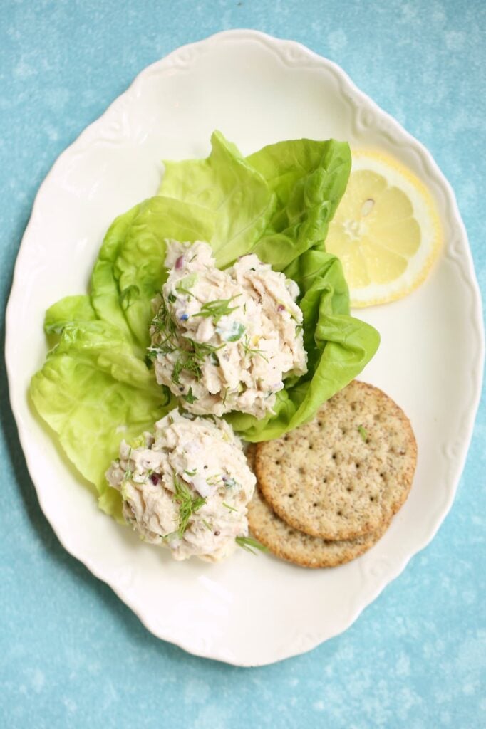 A portrait view of chicken salad served in lettuce cups with crackers and lemon.