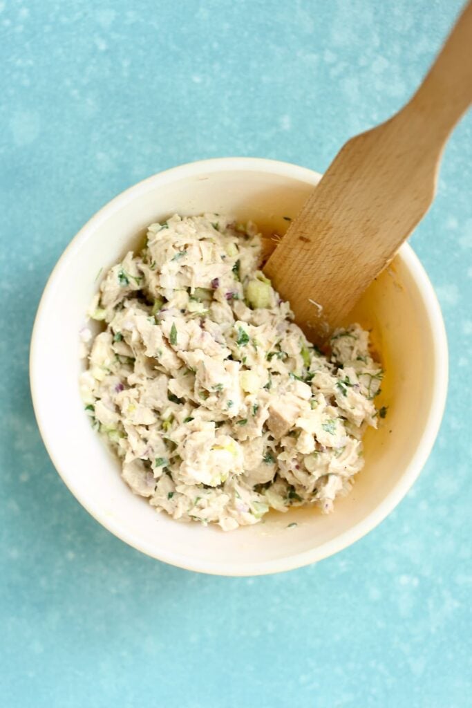 A mixing bowl and wooden mixer of chicken salad in a bowl.