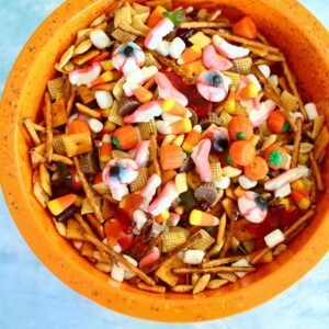 A large orange bowl of snack mix with pretzels, crackers and candy.