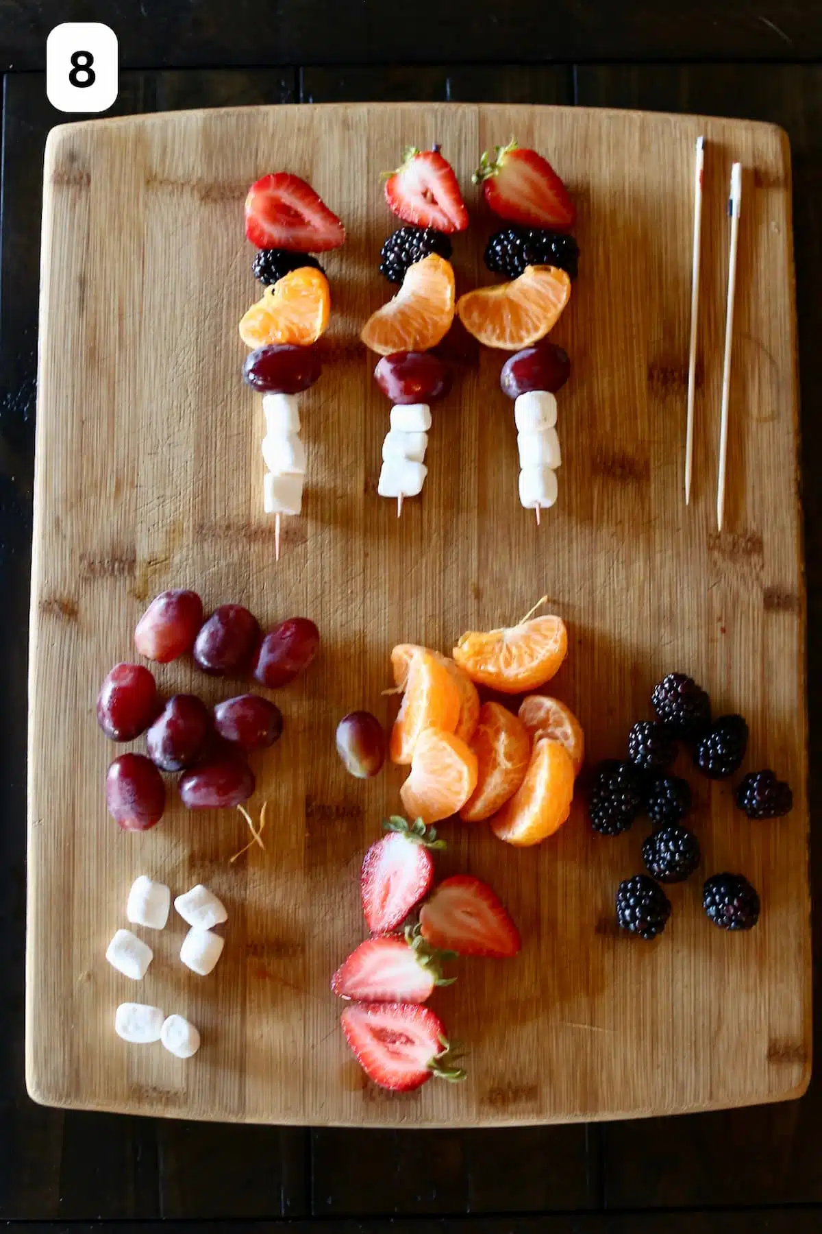 a cutting board with fruit snacks on sticks.