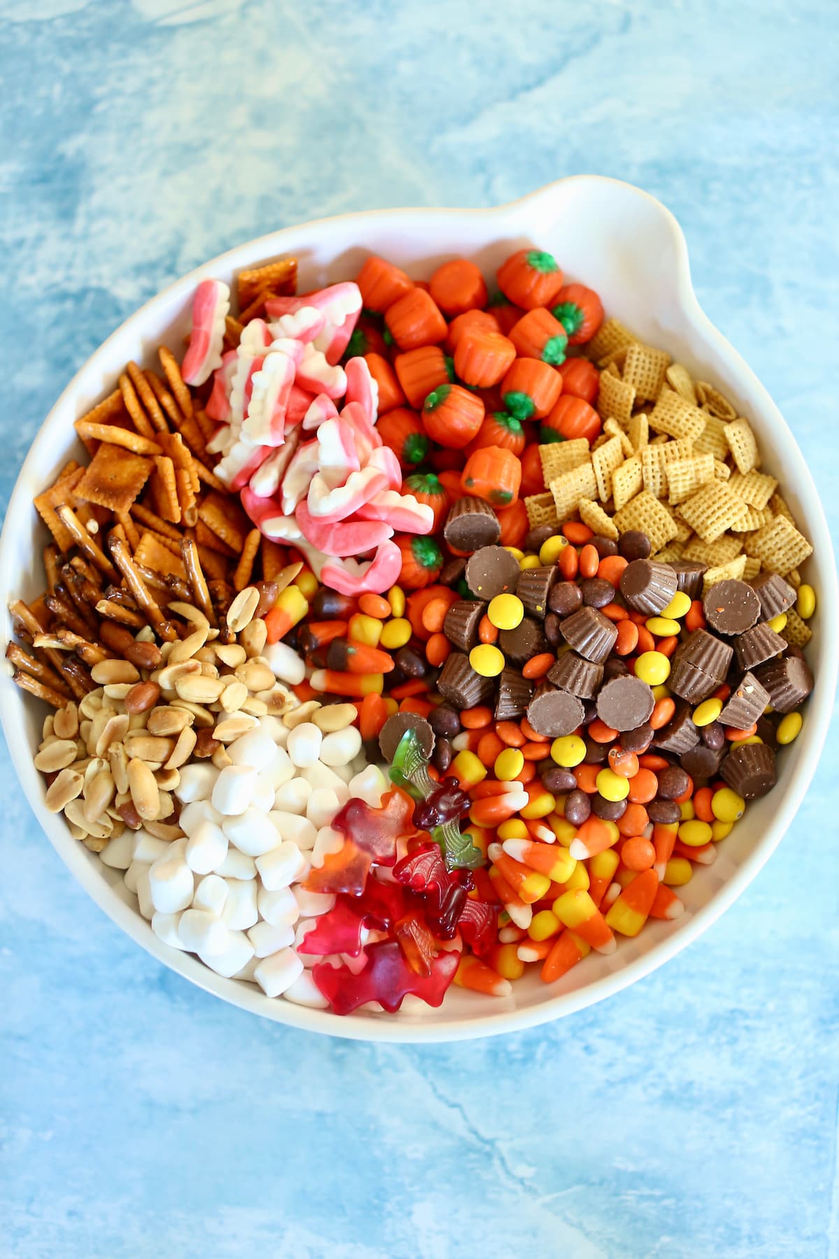 A large bowl of fall snack mix ingredients like pretzels, cheese crackers, peanuts and seasonal candy.