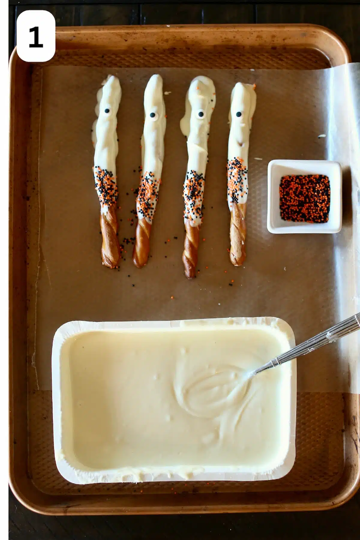 Stick pretzels are dipped in white chocolate and sprinkles with candy eyes.