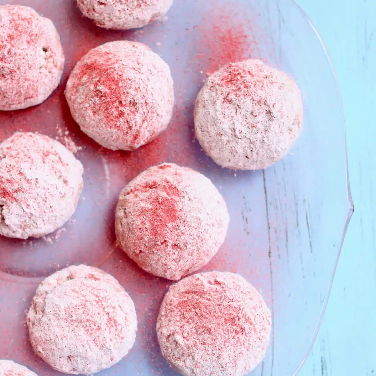 a close-up photo of pink butterball cookies on a blue backdrop.